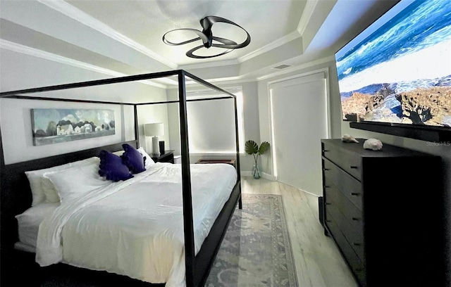 bedroom with light wood finished floors, a tray ceiling, visible vents, and crown molding