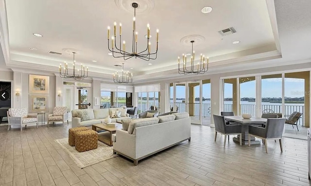 living area with a wealth of natural light, a tray ceiling, visible vents, and an inviting chandelier