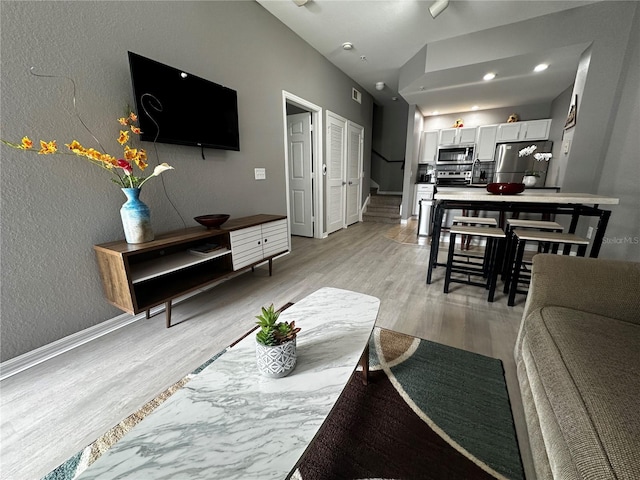 living area featuring light wood finished floors, visible vents, baseboards, a textured wall, and stairway