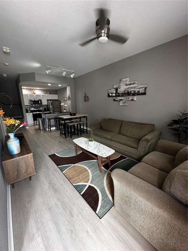 living room featuring ceiling fan, a textured ceiling, wood finished floors, and track lighting