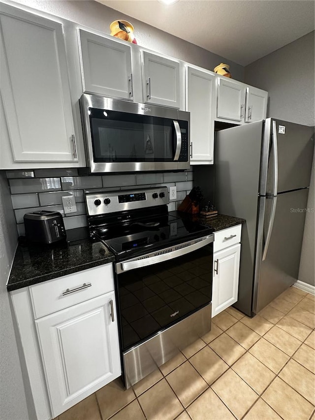 kitchen featuring decorative backsplash, white cabinetry, stainless steel appliances, and dark stone countertops