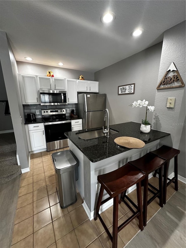 kitchen featuring white cabinetry, a kitchen breakfast bar, appliances with stainless steel finishes, tasteful backsplash, and dark countertops