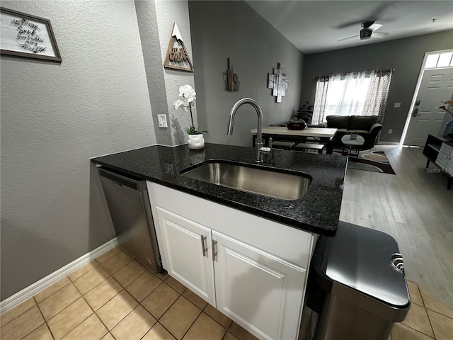 kitchen featuring stainless steel dishwasher, open floor plan, white cabinetry, a sink, and dark stone countertops