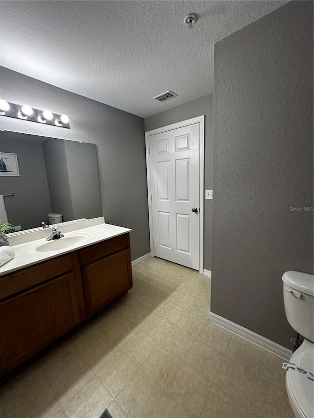 half bath featuring baseboards, a textured wall, toilet, tile patterned floors, and vanity