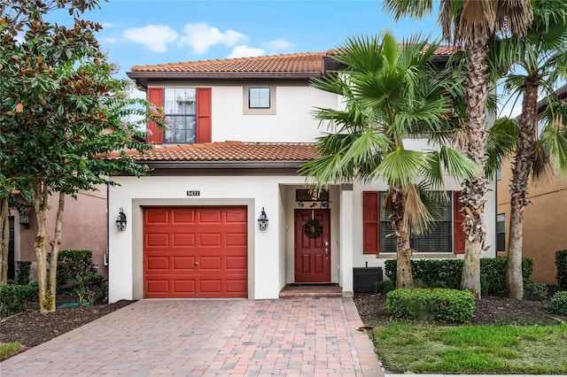 mediterranean / spanish-style house with a garage, a tiled roof, decorative driveway, and stucco siding