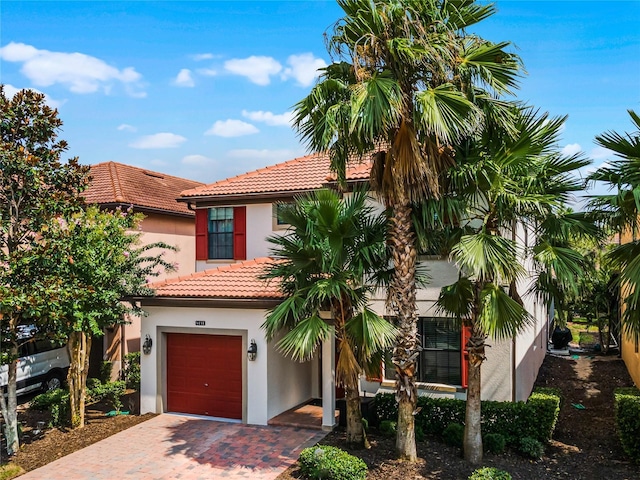 mediterranean / spanish-style house with decorative driveway, a tiled roof, an attached garage, and stucco siding