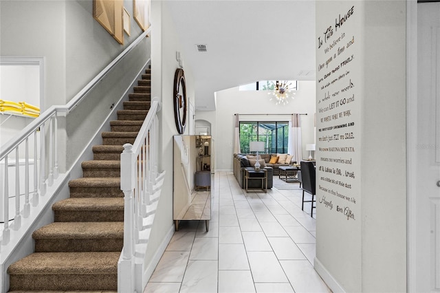 staircase with a chandelier, a high ceiling, visible vents, baseboards, and tile patterned floors