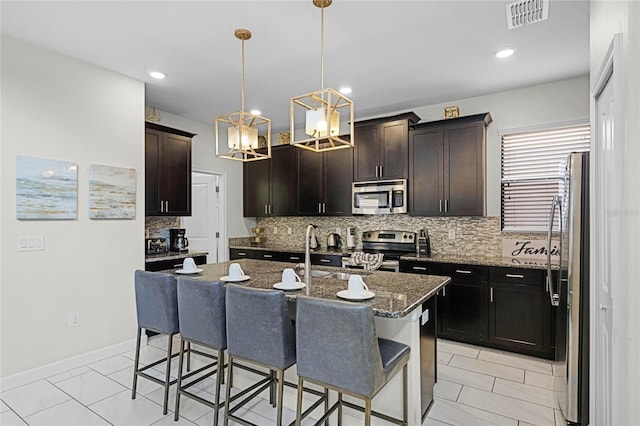 kitchen with a breakfast bar, a sink, visible vents, appliances with stainless steel finishes, and a center island with sink