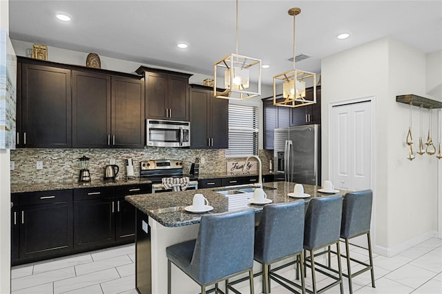 kitchen with visible vents, an island with sink, decorative light fixtures, stainless steel appliances, and a sink