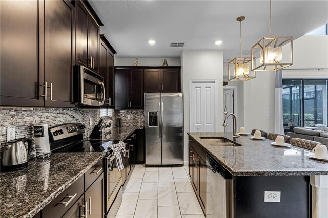 kitchen with visible vents, appliances with stainless steel finishes, a sink, an island with sink, and dark stone counters