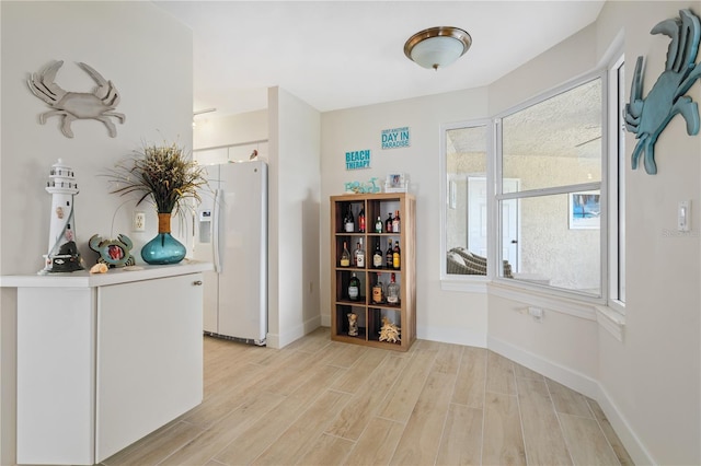 interior space with light wood-type flooring, white refrigerator with ice dispenser, and baseboards