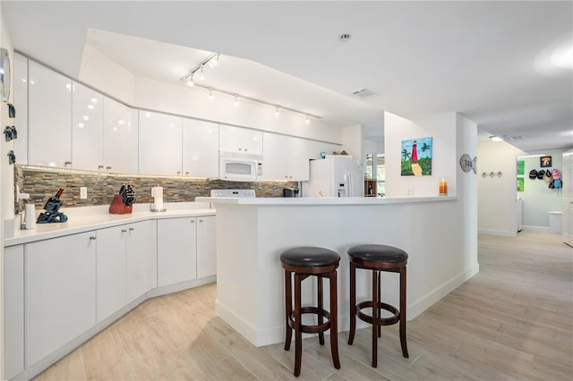 kitchen featuring white appliances, a kitchen bar, white cabinetry, and backsplash