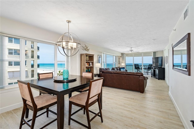 dining area featuring visible vents, a water view, light wood-style floors, a textured ceiling, and baseboards