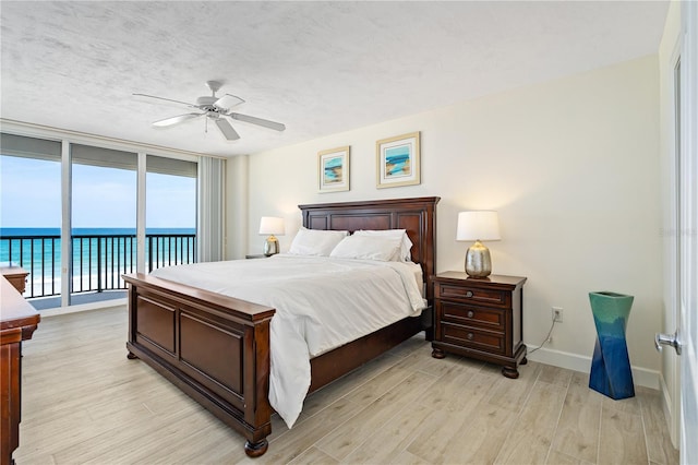 bedroom with floor to ceiling windows, light wood finished floors, a water view, a textured ceiling, and access to outside