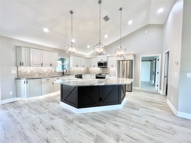 kitchen with light wood-type flooring, a large island, stainless steel appliances, light stone countertops, and decorative backsplash