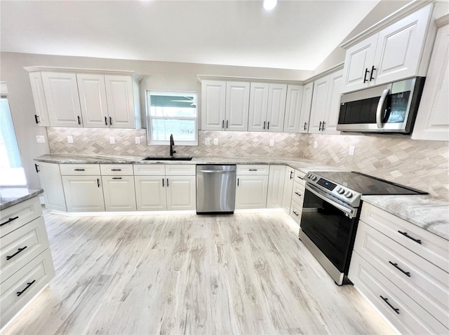 kitchen featuring appliances with stainless steel finishes, sink, vaulted ceiling, and light hardwood / wood-style floors