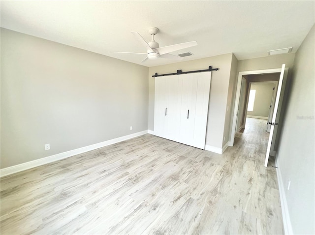 unfurnished bedroom featuring ceiling fan, a barn door, light wood-type flooring, and a closet