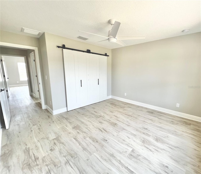 unfurnished bedroom featuring a textured ceiling, a barn door, ceiling fan, and light hardwood / wood-style floors