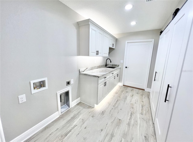 laundry area with a barn door, cabinets, electric dryer hookup, sink, and light hardwood / wood-style flooring