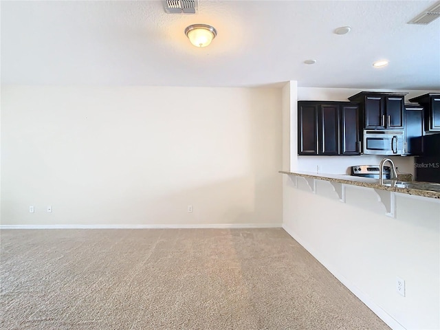 kitchen featuring light stone counters, stove, black refrigerator, a breakfast bar area, and light colored carpet