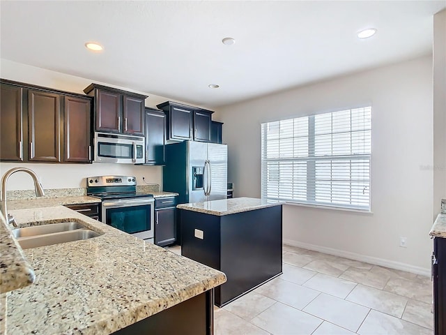 kitchen featuring dark brown cabinets, stainless steel appliances, light stone counters, a center island, and sink