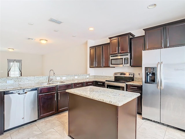 kitchen featuring appliances with stainless steel finishes, light stone countertops, sink, light tile patterned flooring, and a center island