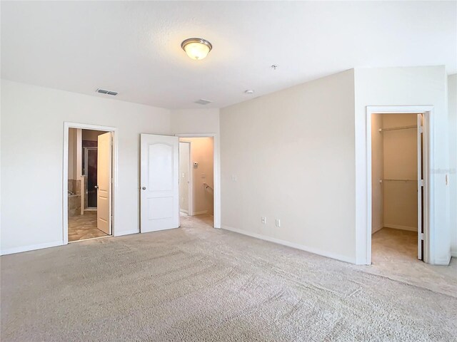 unfurnished bedroom with a spacious closet, a closet, connected bathroom, and light colored carpet