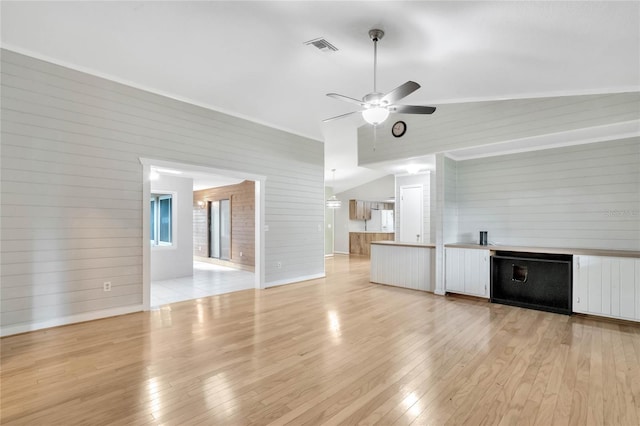 unfurnished living room with ceiling fan, light wood-type flooring, vaulted ceiling, and wooden walls