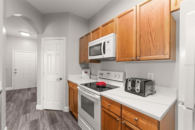 8105 Coconut Palm Way Unit 203, Kissimmee, FL 34747 - kitchen with white appliances, arched walkways, dark wood-style flooring, light countertops, and brown cabinets