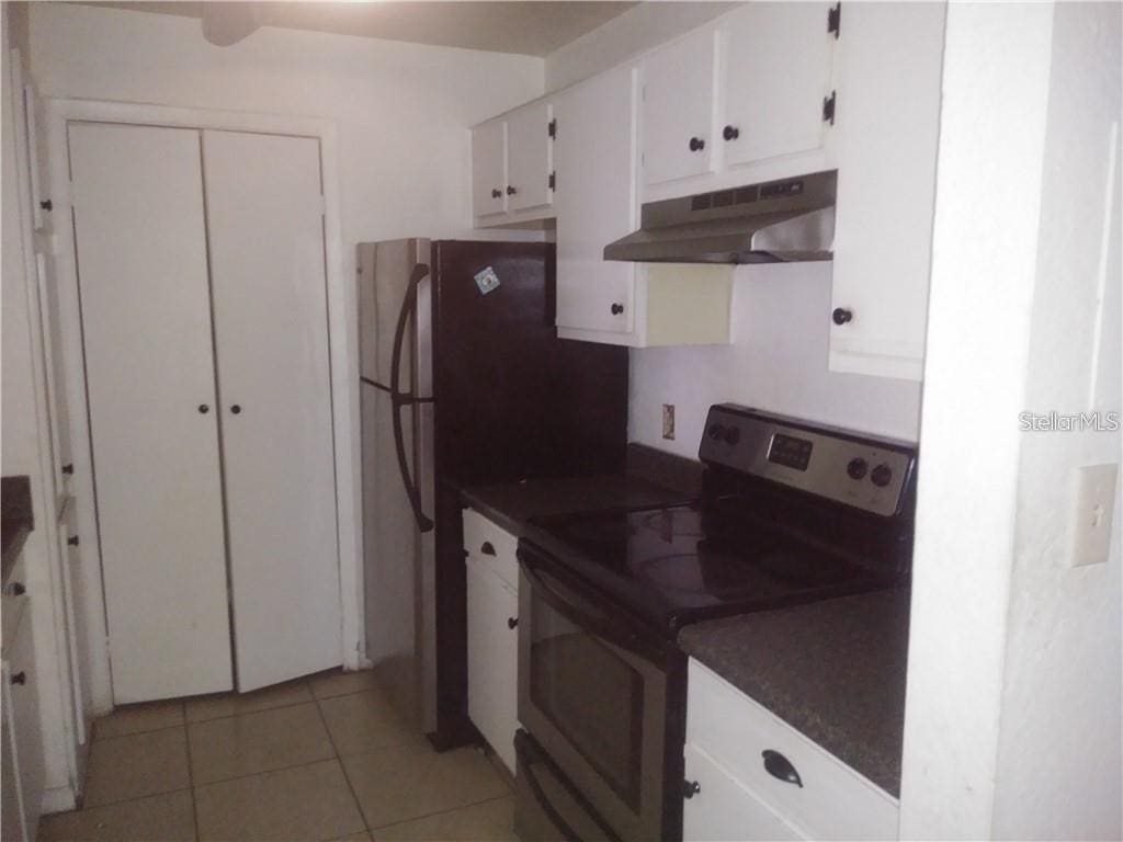 kitchen with light tile patterned floors, white cabinets, range with electric stovetop, and wall chimney exhaust hood