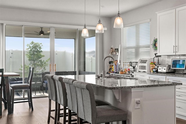 kitchen featuring dark stone counters, backsplash, sink, decorative light fixtures, and ceiling fan