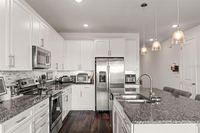 kitchen with sink, dark stone countertops, appliances with stainless steel finishes, dark wood-type flooring, and a kitchen island with sink