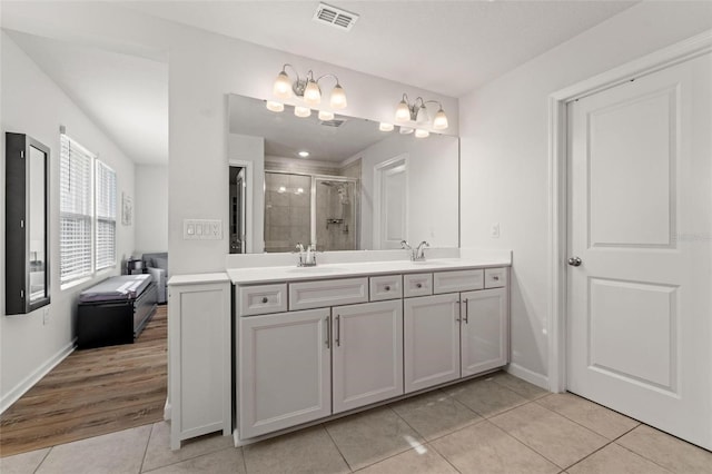 bathroom with a shower with shower door, dual bowl vanity, and tile patterned floors