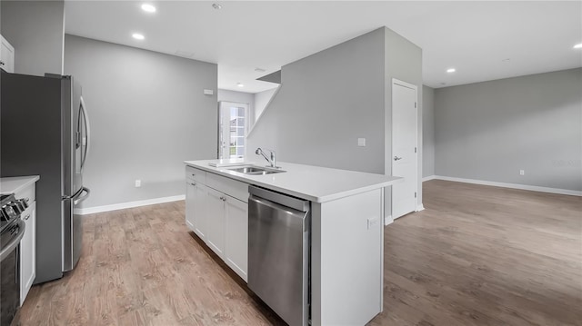 kitchen featuring light wood-style flooring, a sink, white cabinetry, appliances with stainless steel finishes, and an island with sink