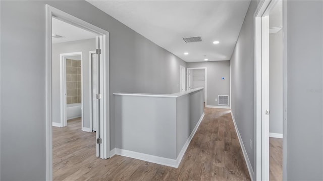 corridor with wood finished floors, visible vents, and baseboards