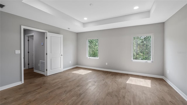 spare room featuring visible vents, a tray ceiling, baseboards, and wood finished floors