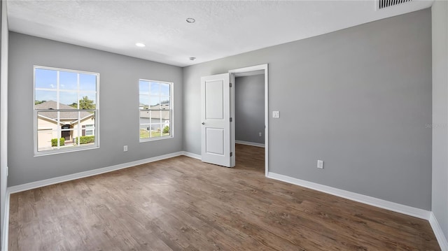 spare room with a textured ceiling, wood finished floors, visible vents, and baseboards