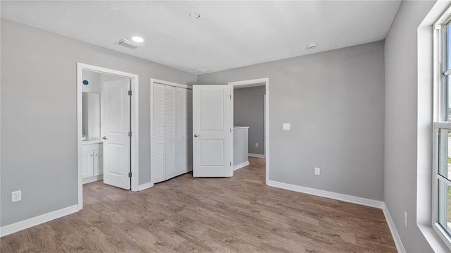 unfurnished bedroom with connected bathroom, wood finished floors, visible vents, baseboards, and a closet