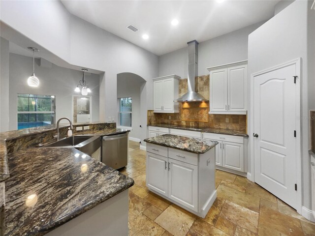 kitchen with dishwasher, backsplash, wall chimney range hood, a kitchen island, and decorative light fixtures