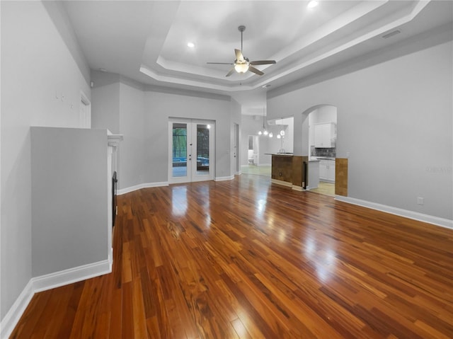 unfurnished living room featuring wood finished floors, a ceiling fan, baseboards, french doors, and a tray ceiling