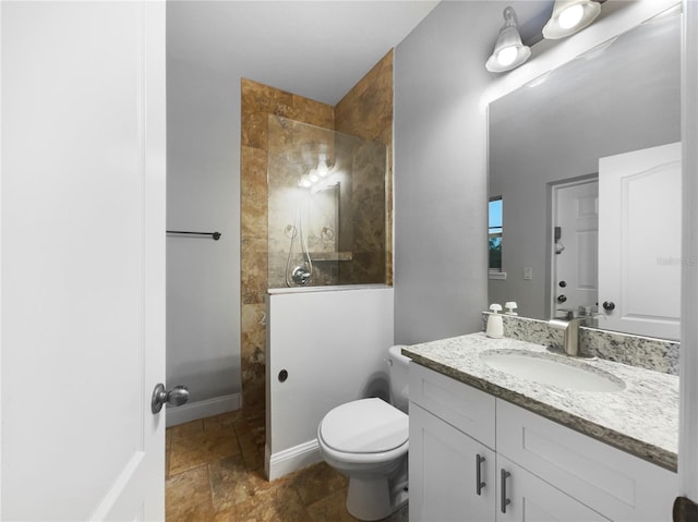 bathroom featuring stone tile flooring, toilet, vanity, a walk in shower, and baseboards