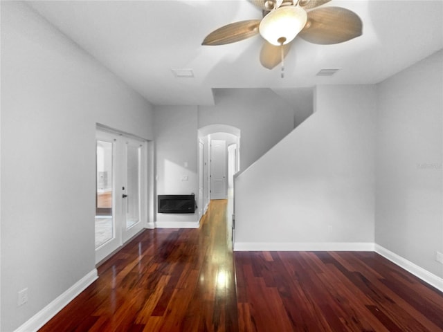 unfurnished living room featuring a ceiling fan, visible vents, baseboards, dark wood-style floors, and a glass covered fireplace