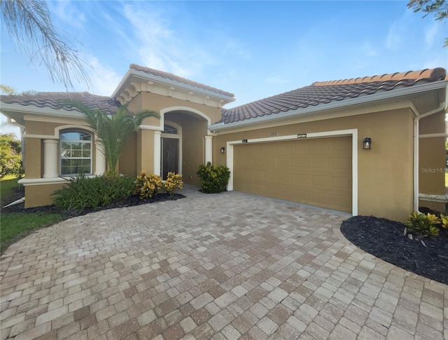 view of front facade featuring a garage, a tiled roof, decorative driveway, and stucco siding