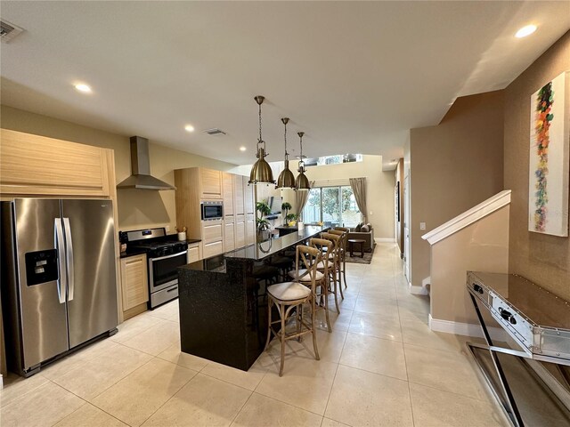 kitchen with wall chimney exhaust hood, a center island with sink, light tile patterned floors, stainless steel appliances, and a breakfast bar