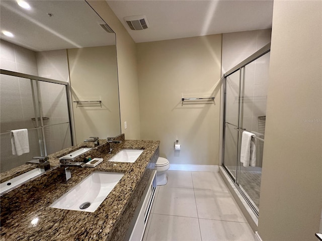 bathroom featuring dual bowl vanity, tile patterned floors, a shower with shower door, and toilet