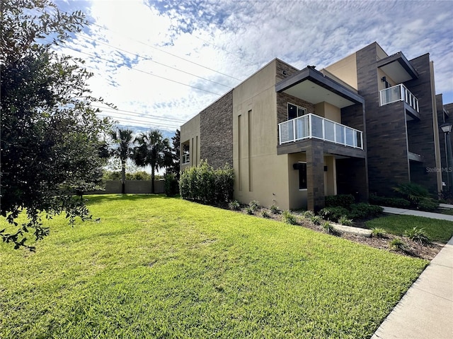 view of side of property with stucco siding, a lawn, and a balcony