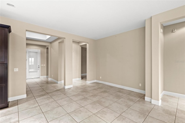 spare room featuring light tile patterned floors, a skylight, and baseboards