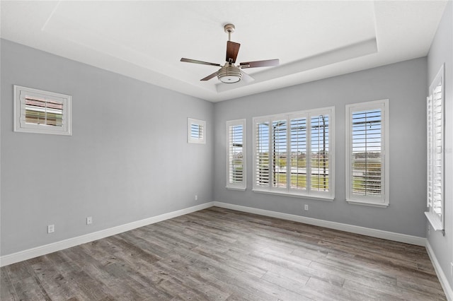 unfurnished room with ceiling fan, a tray ceiling, baseboards, and wood finished floors