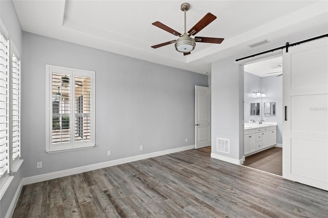 unfurnished bedroom featuring a barn door, wood finished floors, visible vents, and a tray ceiling