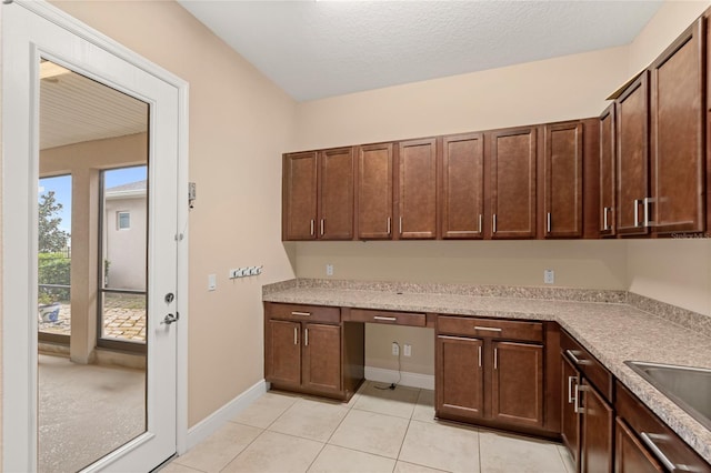 kitchen featuring light tile patterned floors, built in desk, light countertops, and baseboards